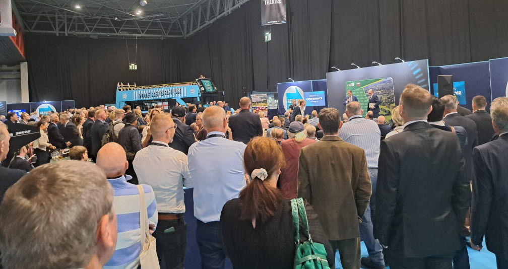 Delegates gather at fringe events in the NEC exhibition hall beside a Vote Reform UK bus.