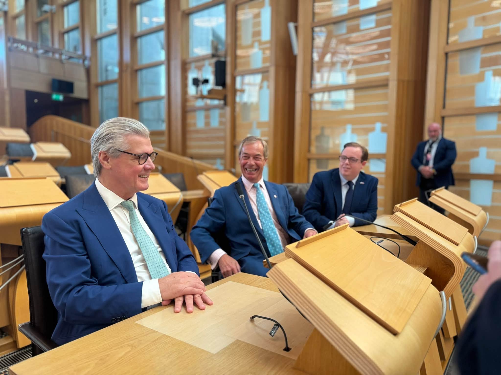 Malcolm Offord and Nigel Farage seated in the Holyrood chamber with a Reform MSP.