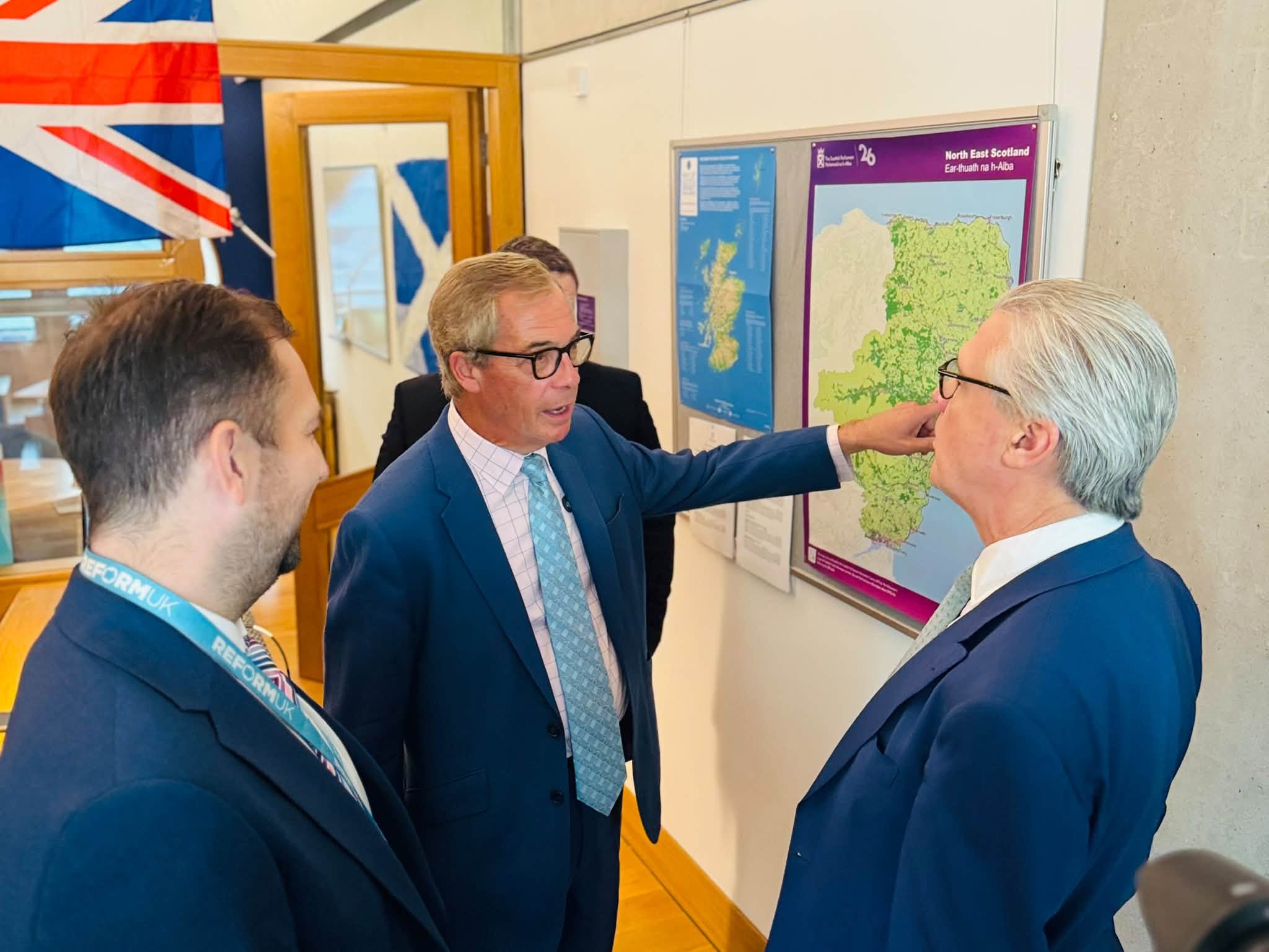 Nigel Farage points to a map of North East Scotland while talking with Malcolm Offord in Reform's Holyrood office, with the Union flag and the Saltire behind them.