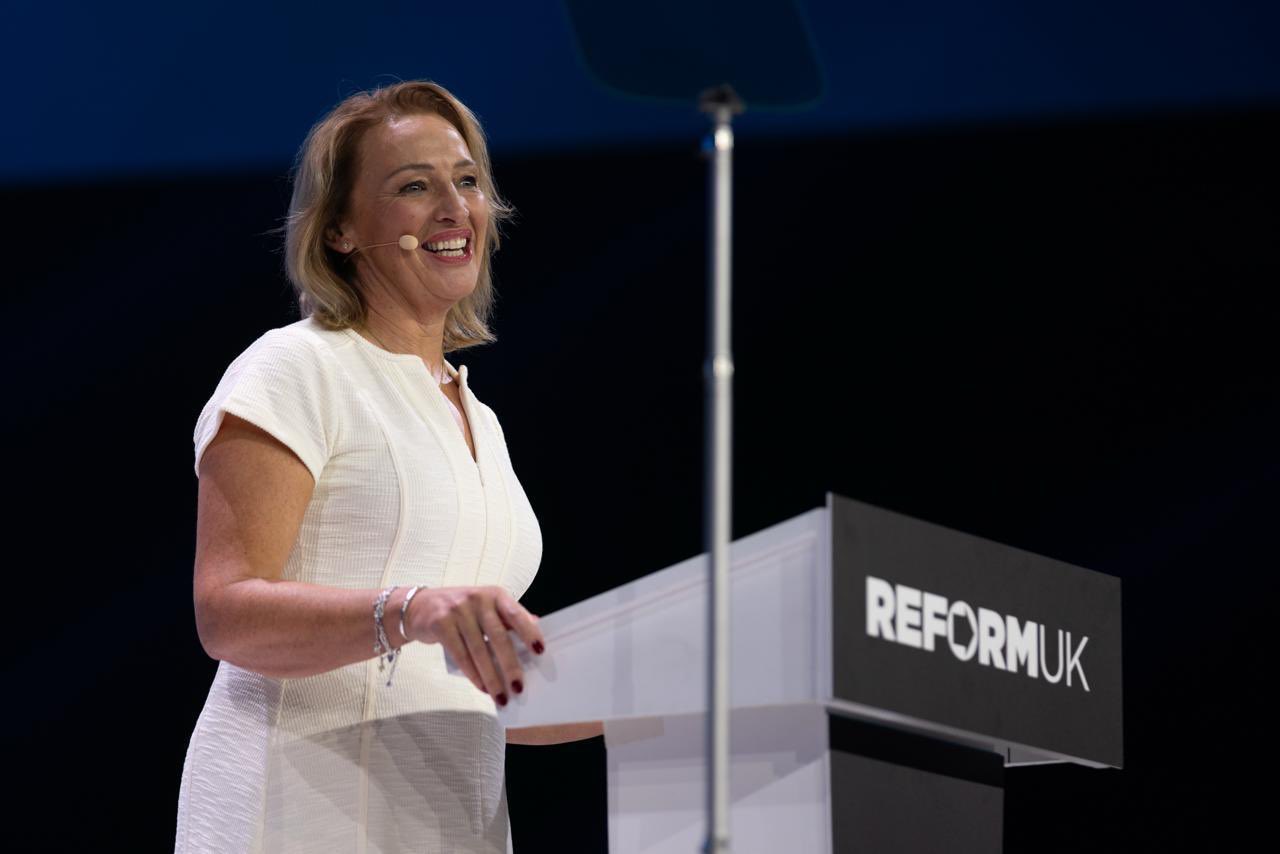 Sarah Pochin speaks at Reform UK Conference 2026 in Birmingham, smiling from the Reform UK podium in a white dress.