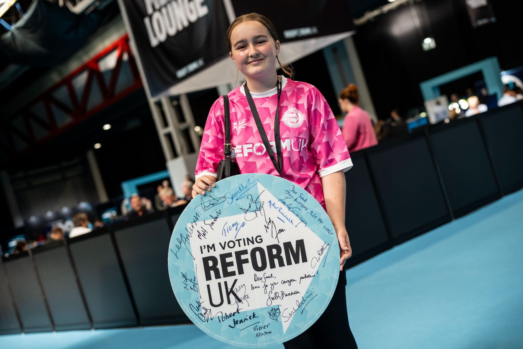 A young Reform UK supporter holds a signed I'm Voting Reform UK sign at Conference 2026.